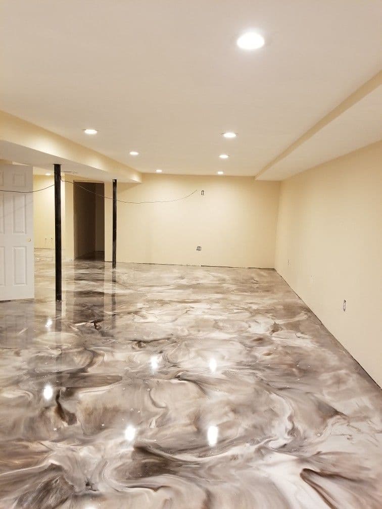 A wide shot of a finished, high-gloss white and grey metallic epoxy floor in a basement, reflecting overhead recessed lighting.