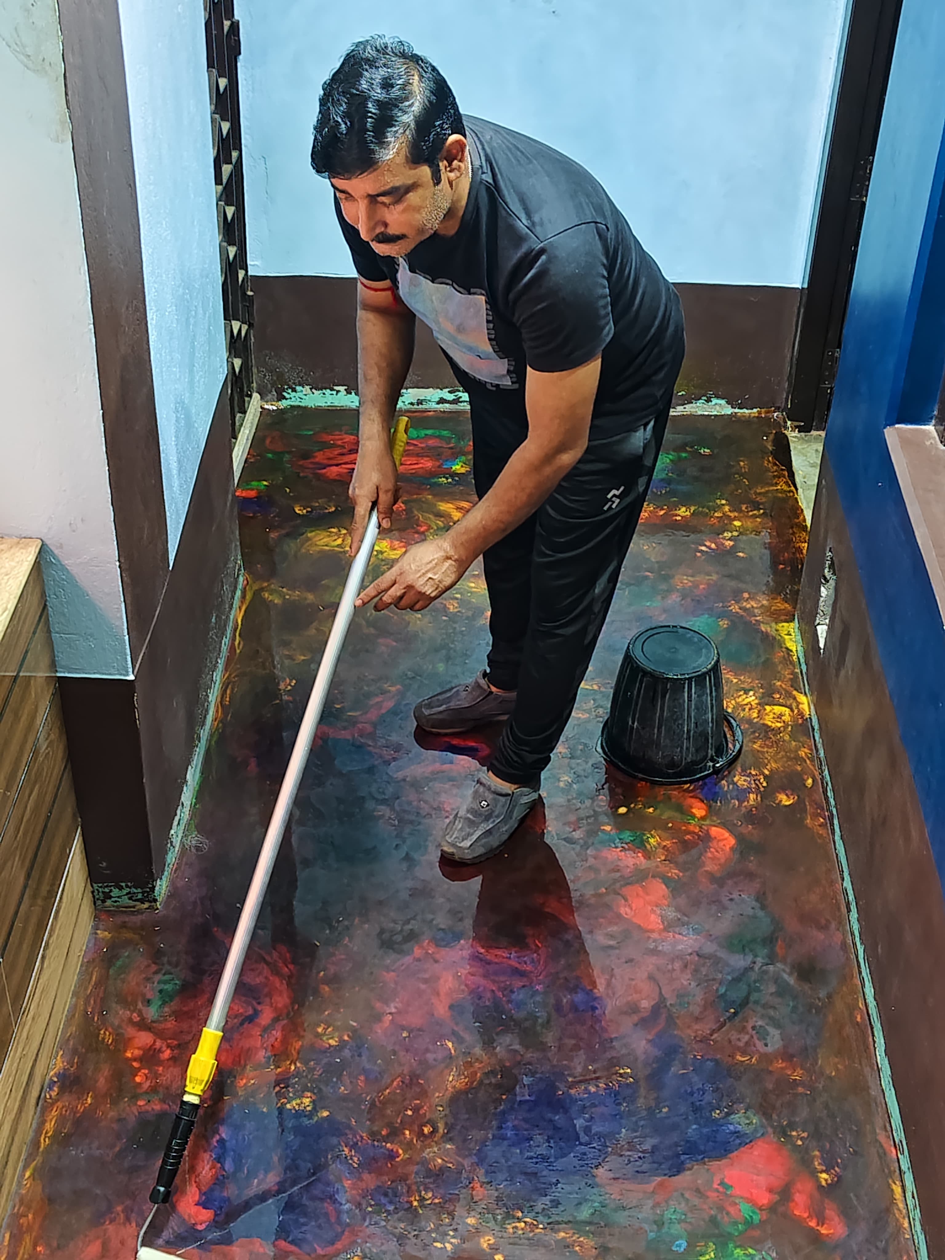 Craftsman spreading multi-coloured metallic epoxy across a corridor floor with a spiked roller